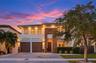 Two-story contemporary exterior featuring a light-toned stucco facade, wood-finish accents, integrated soffit lighting, a two-car garage, and a paver 