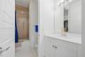 Bathroom featuring a white vanity with a composite countertop, an integrated rectangular sink, a floor-to-ceiling tiled shower surround with a light w