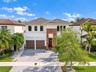 Two-story exterior featuring a stucco facade, wood-slat vertical accents, a concrete tile roof, dual garage doors, and a paver driveway