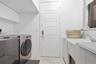 Laundry area featuring white cabinetry, a utility sink with a faucet, five-panel door, and tiled flooring