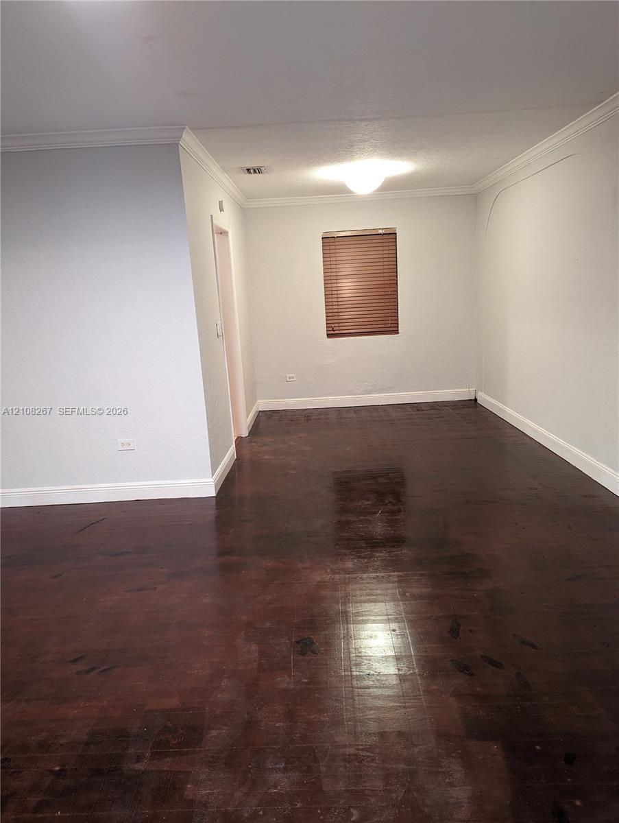 Interior space featuring dark wood-finish flooring, crown molding, and a single window with slatted blinds