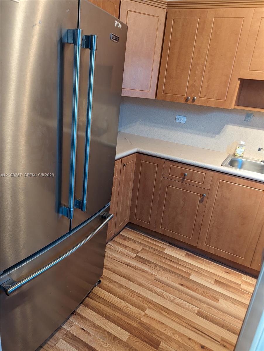 Stainless steel French door refrigerator, wood-finish cabinetry, solid-surface countertops, inset stainless steel sink, and wood-finish flooring
