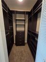 Custom walk-in closet featuring dark-finish built-in cabinetry, integrated shelving, four-drawer chest, and metal garment rods