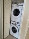 Stacked front-load washer and dryer set, white louvered bifold door, and built-in overhead wire shelving