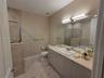 Bathroom featuring a vanity with integrated sink, stone-surface countertop, full-width wall mirror, tile flooring, and walk-in shower with tile surrou