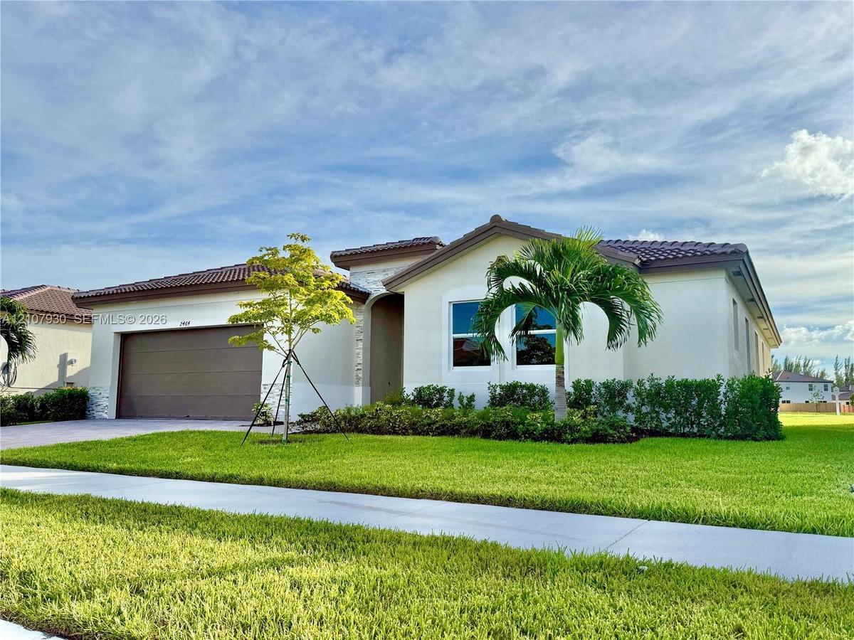 Single-story exterior featuring a tile roof, light-toned stucco facade, stone masonry accents, multi-car garage, and manicured landscaping