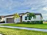 Single-story exterior featuring a tile roof, light-toned stucco facade, stone masonry accents, multi-car garage, and manicured landscaping