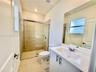 Bathroom featuring a glass-enclosed shower with tile surround, a white vanity with a composite countertop and integrated basin, a large wall-mounted m