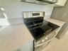 Stainless steel electric range with a smooth cooktop, neutral solid-surface countertops, and sleek flat-panel cabinetry