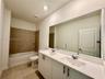 Double vanity featuring white cabinetry, a solid surface countertop, rectangular under-mount sinks, and a full-width mirror, accompanied by a bathtub 