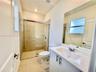 Bathroom featuring a glass-enclosed shower with tile surround, white vanity cabinet with a stone-composite countertop, undermount sink, and large wall