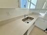 Kitchen featuring white cabinetry with brushed metal hardware, solid-surface countertops, an integrated stainless steel under-mount sink, and ceramic 