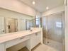 Bathroom featuring a white vanity with a solid-surface countertop, an integrated sink, full-width vanity mirror, walk-in shower with tile surround, an