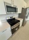 Kitchen featuring flat-panel white cabinetry, stainless steel microwave, glass-top electric range, stainless steel refrigerator, and neutral-toned flo