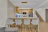 Kitchen featuring light wood-finish cabinetry, waterfall-edge stone countertop, decorative tile backsplash, integrated stainless steel appliances, and