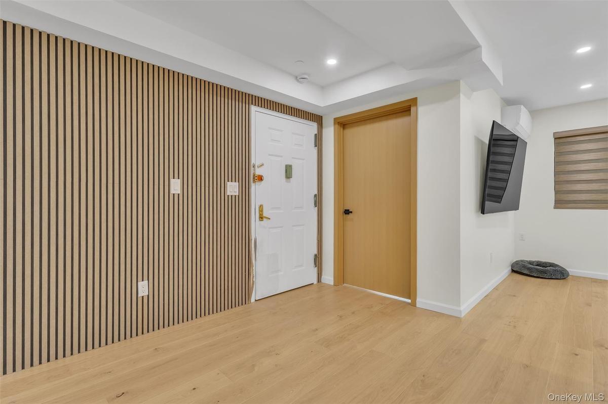 Wood-slat accent wall, light-toned wood-finish flooring, recessed ceiling lighting, and solid-core interior doors