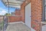 Balcony featuring red brick exterior walls, stone-finish tile flooring, metal railing, and a fixed overhead awning