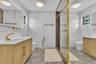 Bathroom featuring light wood-finish vanities with rectangular integrated sinks, gold-tone fixtures, floor-to-ceiling white tiled walls with veining, 