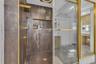 Walk-in shower featuring large-format metallic-finish wall tiles, built-in recessed shelving, gold-tone hardware, and a frameless glass door enclosure