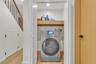 Laundry closet featuring a stainless-steel washer-dryer combination unit, custom built-in wood shelving, wood-finish flooring, and double-hinged doors
