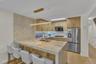 Kitchen featuring a waterfall-edge island with stone-finish countertops, wood-finish cabinetry, a tiled backsplash, wood-finish flooring, and a linear