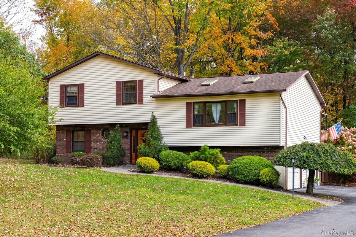 Home surrounded by mature trees and landscaping, featuring a paved driveway and an expansive front lawn