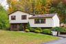Home surrounded by mature trees and landscaping, featuring a paved driveway and an expansive front lawn