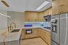 Kitchen featuring light wood-finish cabinetry, stone-patterned countertops, a textured mosaic backsplash, an undermount stainless steel sink with a hi