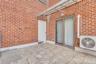Outdoor terrace featuring red brick walls, tiled flooring, a sliding glass door, an attached metal awning, and wall-mounted exterior lighting