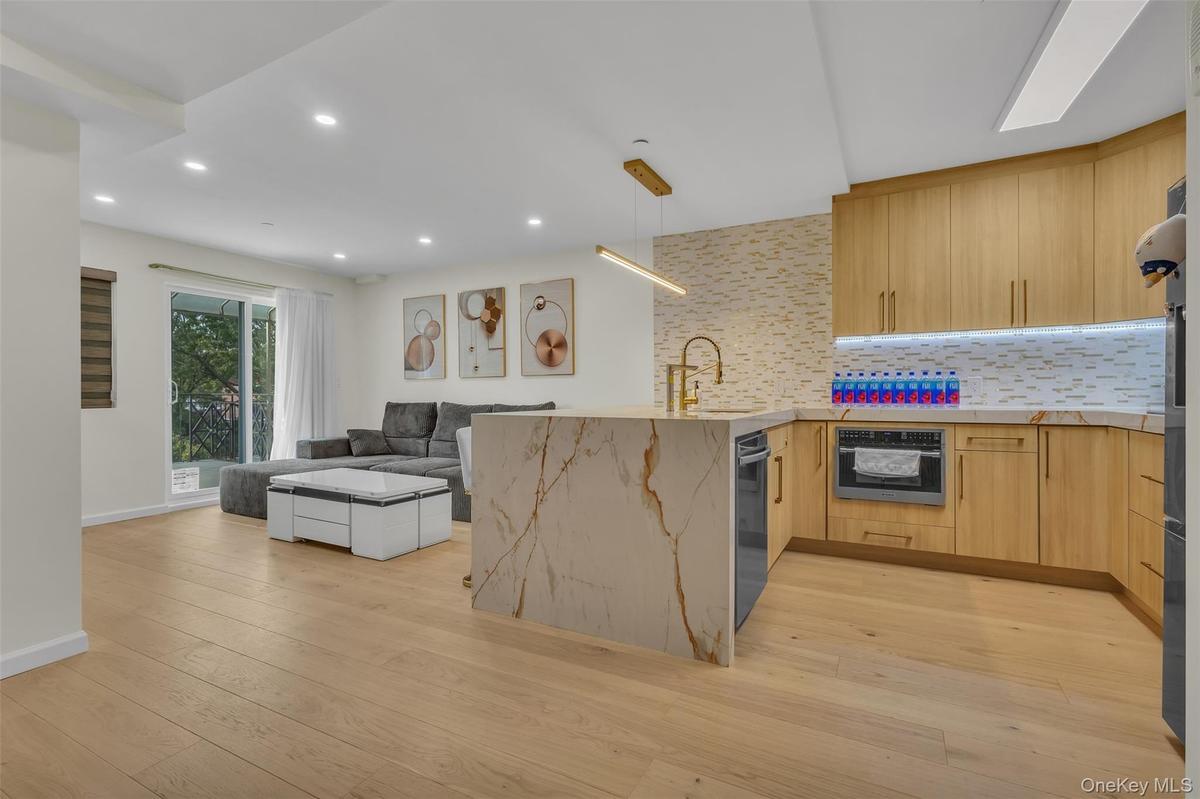 Kitchen featuring wood-finish cabinetry, stone-pattern waterfall island, recessed lighting, integrated under-cabinet lighting, and glass tile backspla