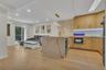 Kitchen featuring wood-finish cabinetry, stone-pattern waterfall island, recessed lighting, integrated under-cabinet lighting, and glass tile backspla