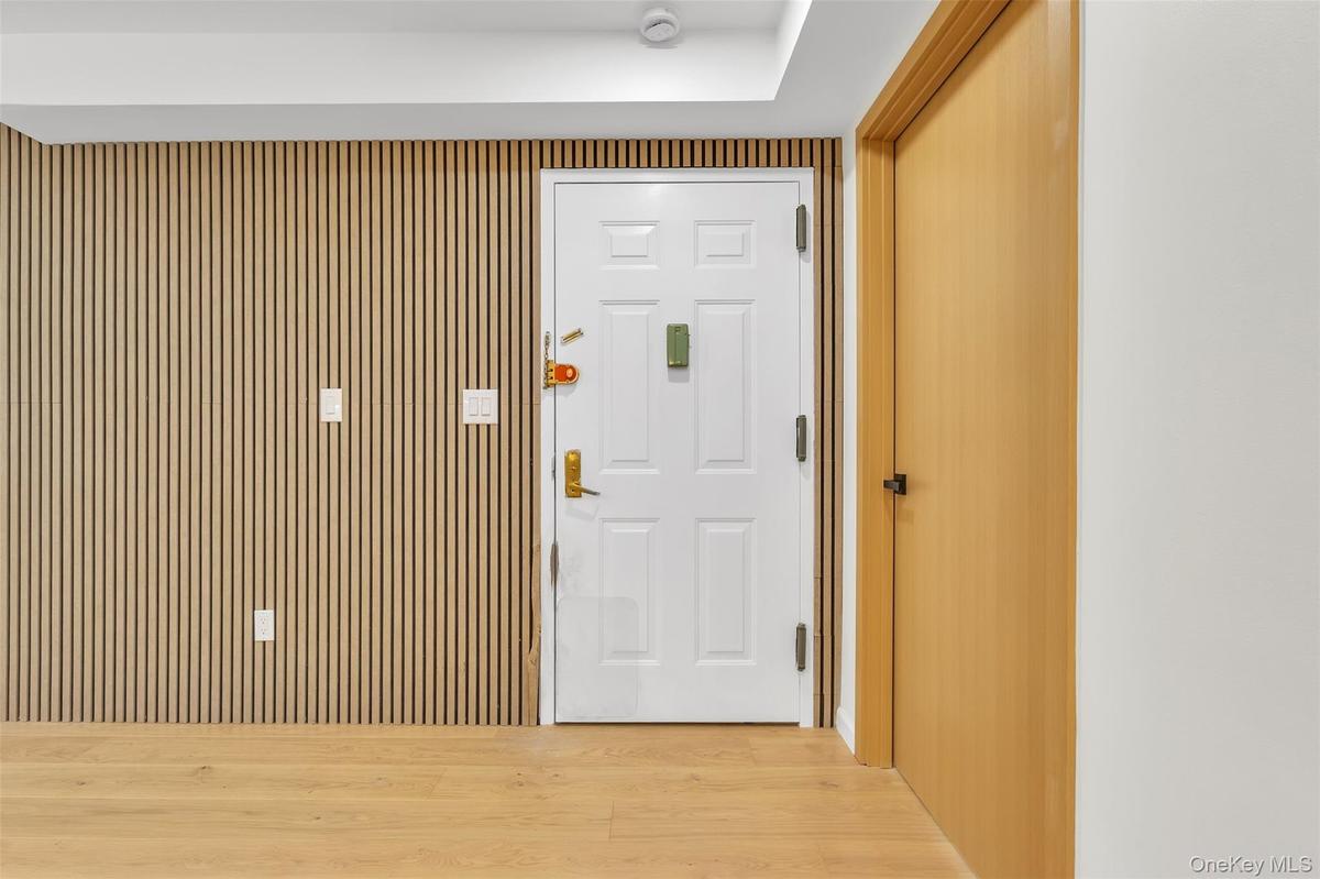 Vertical wood-slat wall paneling, white six-panel entry door with brass-finish hardware, wood-finish flooring, and solid-core interior door with match