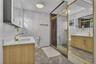 Bathroom featuring wood-finish cabinetry, white solid-surface countertops, gold-toned hardware, full-height tile wall cladding, and a glass-enclosed s
