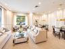 Expansive living space featuring neutral-toned carpeting, recessed ceiling lighting, textured wall detailing, and dual circular gold-tone pendant fixt