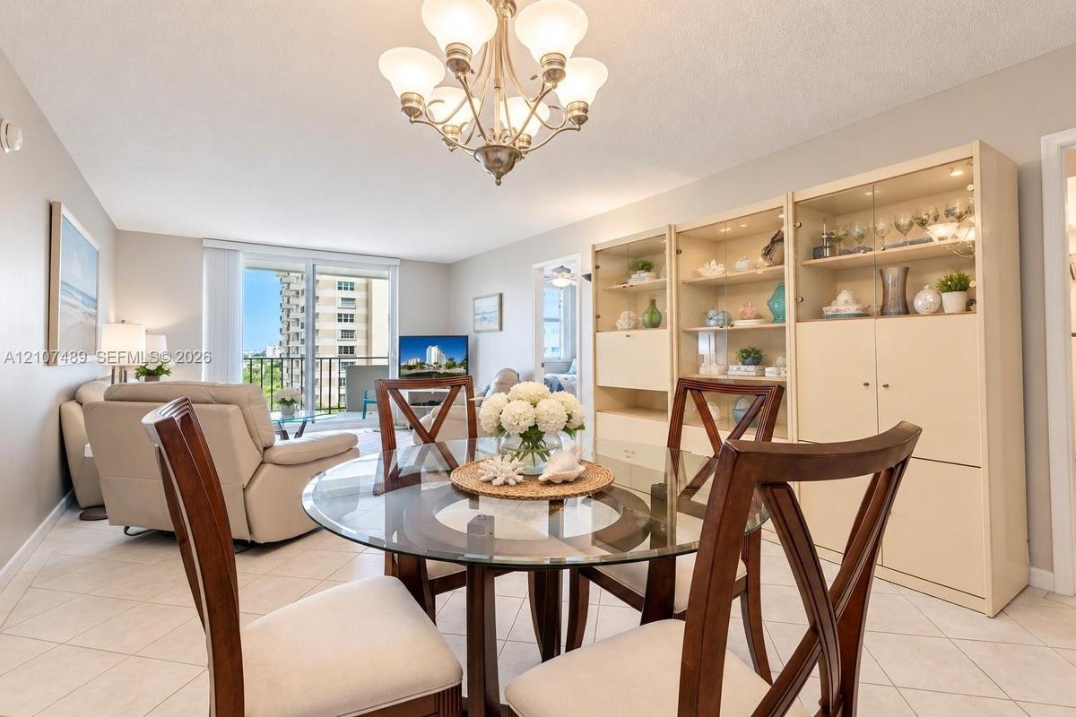 Living area featuring light-toned tile flooring, a multi-bulb chandelier, built-in floor-to-ceiling cabinetry with glass shelving, and sliding glass d