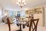 Living area featuring light-toned tile flooring, a multi-bulb chandelier, built-in floor-to-ceiling cabinetry with glass shelving, and sliding glass d