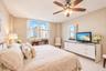 Neutral-toned room featuring large windows, light-colored tile flooring, and a ceiling-mounted fan with integrated lighting