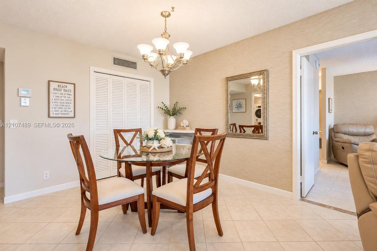 Dining area featuring textured wall finish, ceramic tile flooring, a multi-light metal chandelier, and a louvered-door storage closet