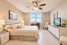 Neutral-toned interior space featuring large windows, textured wall surfacing, neutral tile flooring, and a multi-blade ceiling fan with integrated li