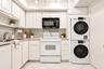 Kitchen featuring shaker-style cabinetry, solid-surface countertops, stainless steel sink with high-arc faucet, integrated laundry center, and tile fl