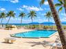 Swimming pool with tile edging, surrounding paver patio, and multiple blue-canopy cabanas situated near the coastline