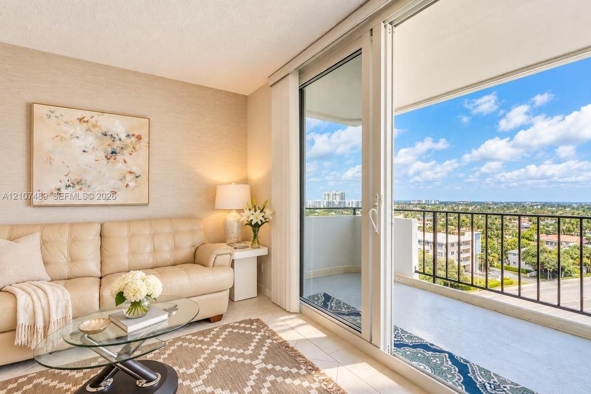 Floor-to-ceiling sliding glass doors opening to a private balcony with metal railing, neutral textured wall covering, and light-toned tile flooring