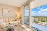 Floor-to-ceiling sliding glass doors opening to a private balcony with metal railing, neutral textured wall covering, and light-toned tile flooring