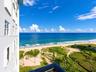 High-rise building exterior featuring a balcony with a black railing, overlooking an expansive coastal shoreline, sandy beach, and native vegetation