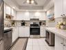 Kitchen featuring white shaker-style cabinetry, stainless steel appliances, recessed ceiling lighting, light-toned tiled flooring, and a peninsula cou