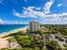 Aerial perspective featuring direct oceanfront access, sandy shoreline, mature tropical landscaping, and paved parking area