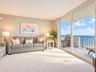Living area featuring wall-to-wall carpeting and floor-to-ceiling sliding glass doors opening to a balcony with metal railings and coastal surrounding