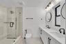 Dual vanity with integrated sinks and black matte faucets, glass-enclosed shower with a rainfall showerhead, white chevron-patterned vanity cabinetry,