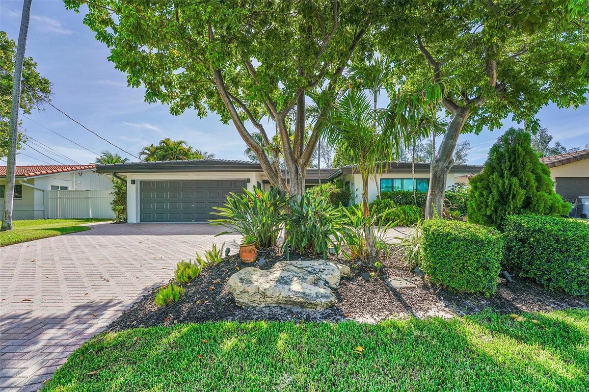 Paver driveway and lush tropical landscaping with mature trees and shrubs