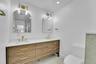 Dual vessel sinks, wood-finish vanity with drawer storage, polished brass fixtures, arched mirrors, and recessed lighting